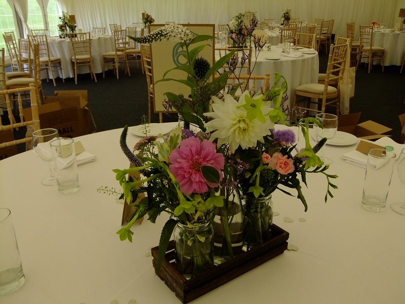A bright and colourful collection of country flowers with feature dahlias in small jars create a striking table centre piece for a rural country wedding. Flowers by Honey Pot Flowers.